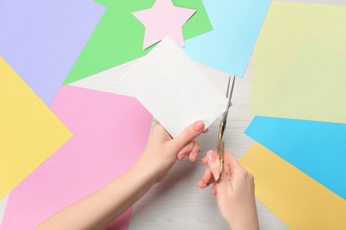 Photo of Woman cutting paper with scissors at white wooden table, top view