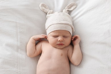 Photo of Adorable little baby with hat sleeping on bed, top view