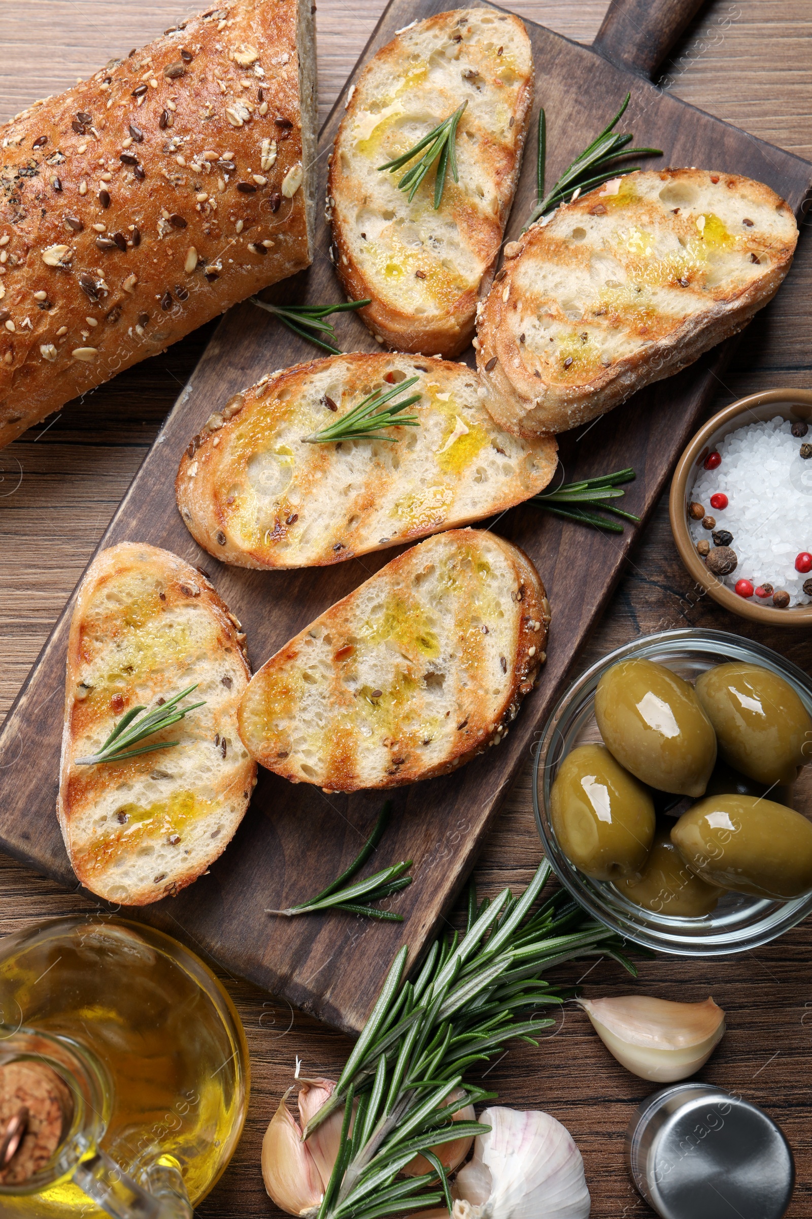 Photo of Tasty bruschettas with oil and rosemary on wooden table, flat lay