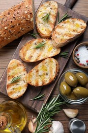 Tasty bruschettas with oil and rosemary on wooden table, flat lay