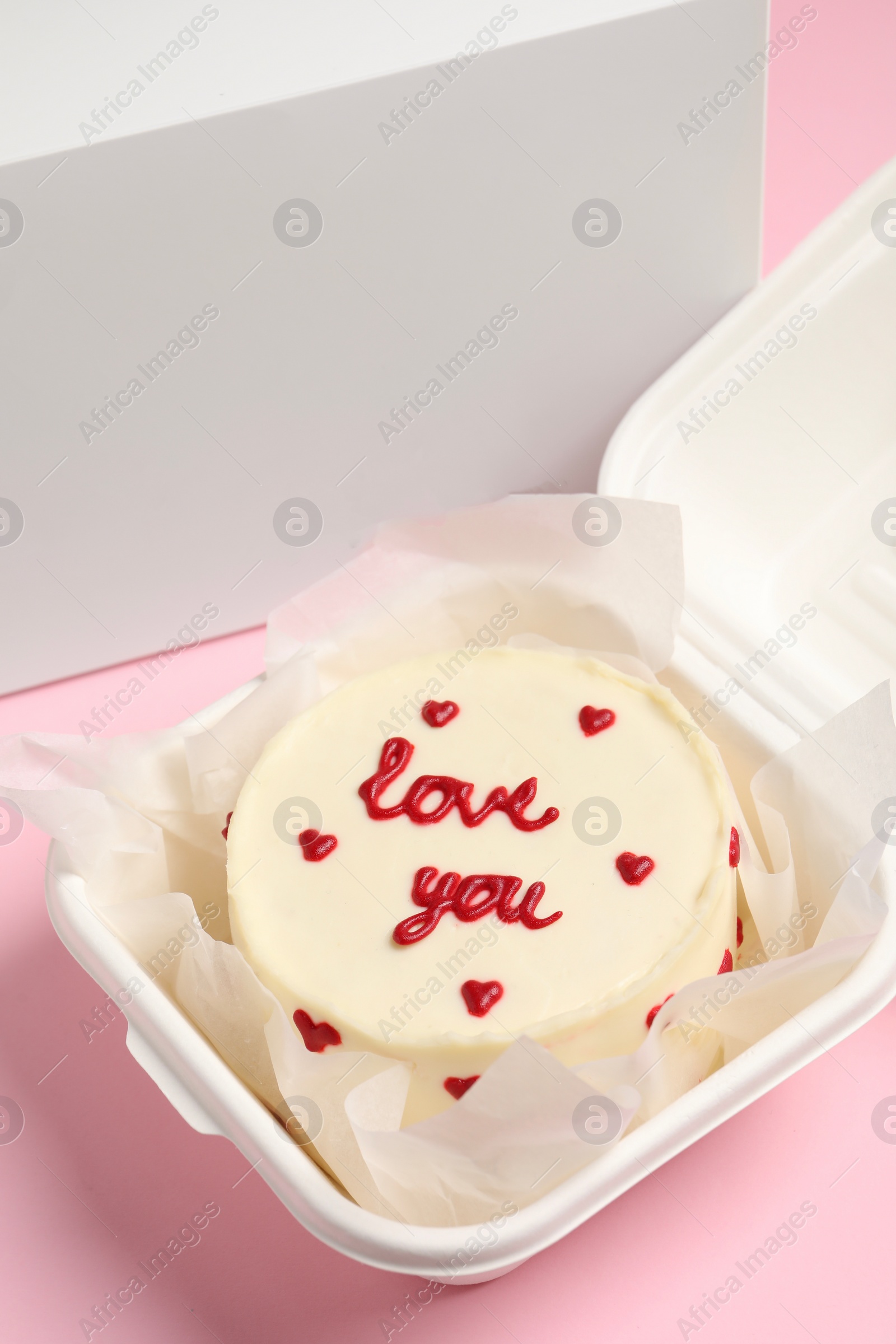 Photo of Tasty bento cake with Love You inscription in takeaway box on pink table