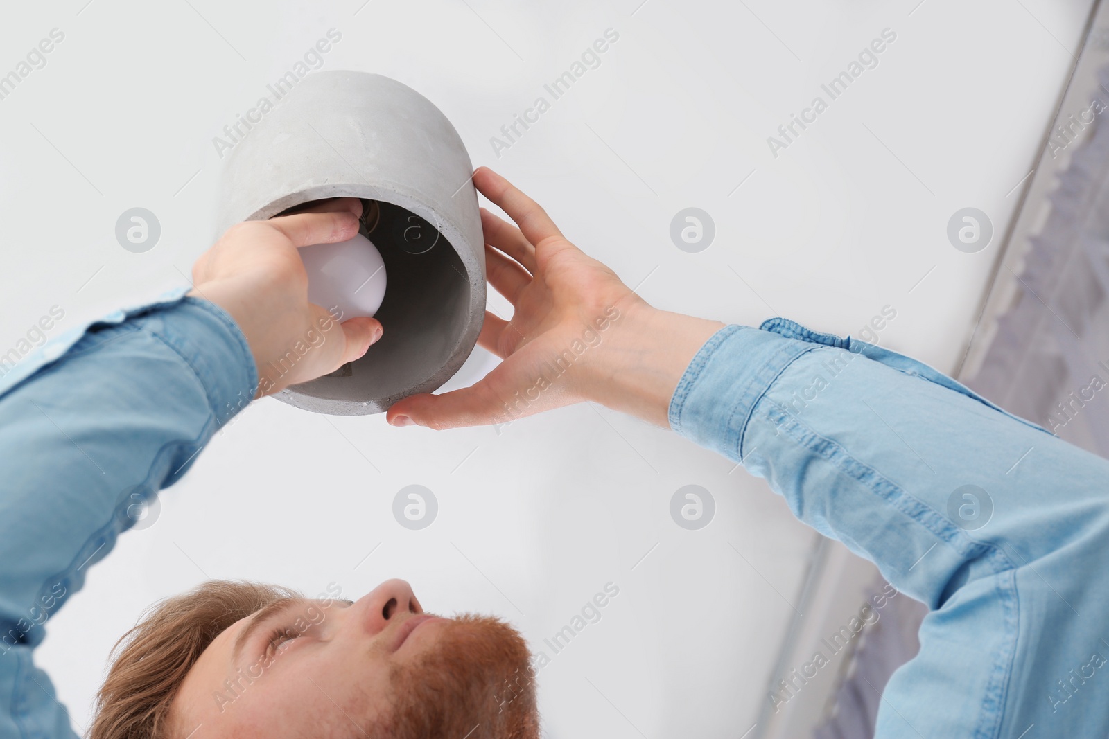 Photo of Man changing light bulb in pendant lamp indoors, low angle view