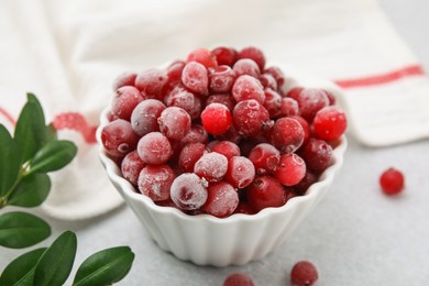 Photo of Frozen red cranberries in bowl and green leaves on light table, closeup