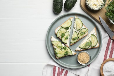 Photo of Tasty cucumber sandwiches with sesame seeds and pea microgreens on white wooden table, flat lay. Space for text