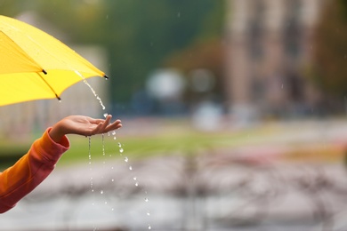 Photo of Woman with yellow umbrella under rain on street, closeup. Space for text