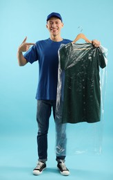 Photo of Dry-cleaning delivery. Happy courier holding dress in plastic bag on light blue background