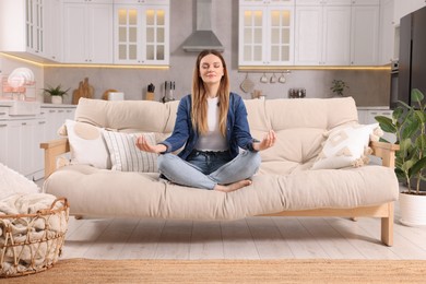 Woman meditating on sofa at home. Harmony and zen