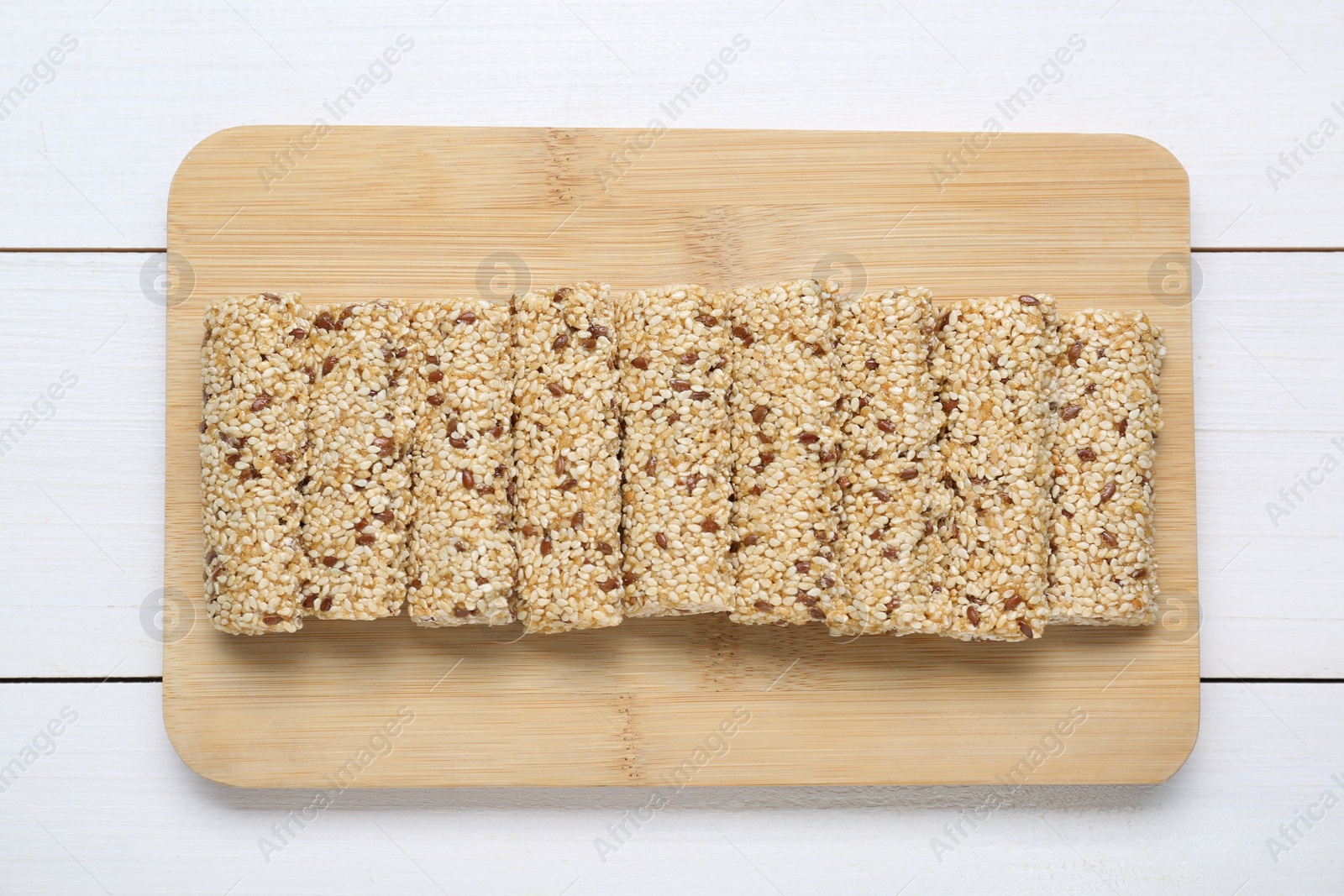 Photo of Tasty sesame seed bars on white wooden table, top view