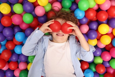 Happy little boy lying on many colorful balls, top view