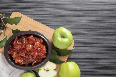 Photo of Bowl of delicious apple jam and fresh fruits on black wooden table, flat lay. Space for text