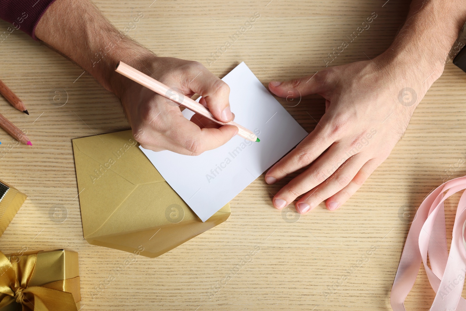 Photo of Man writing message in greeting card at wooden table, top view