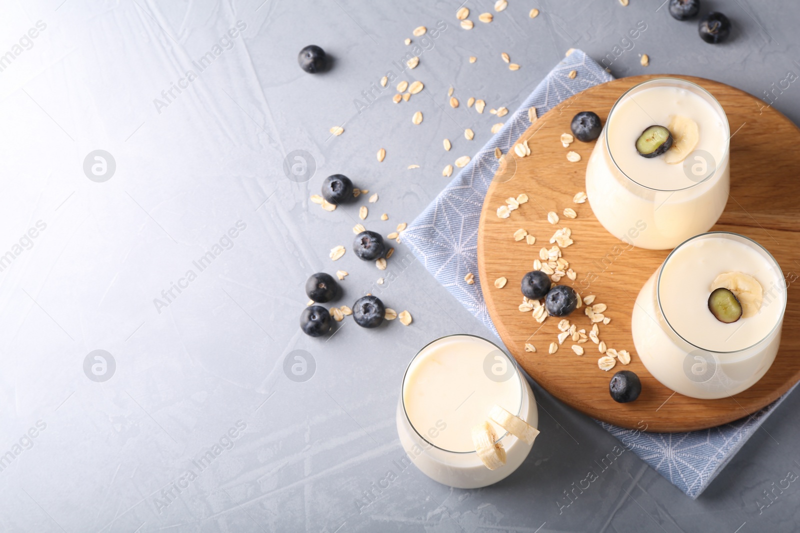 Photo of Tasty yogurt in glasses, oats and blueberries on grey table, above view. Space for text