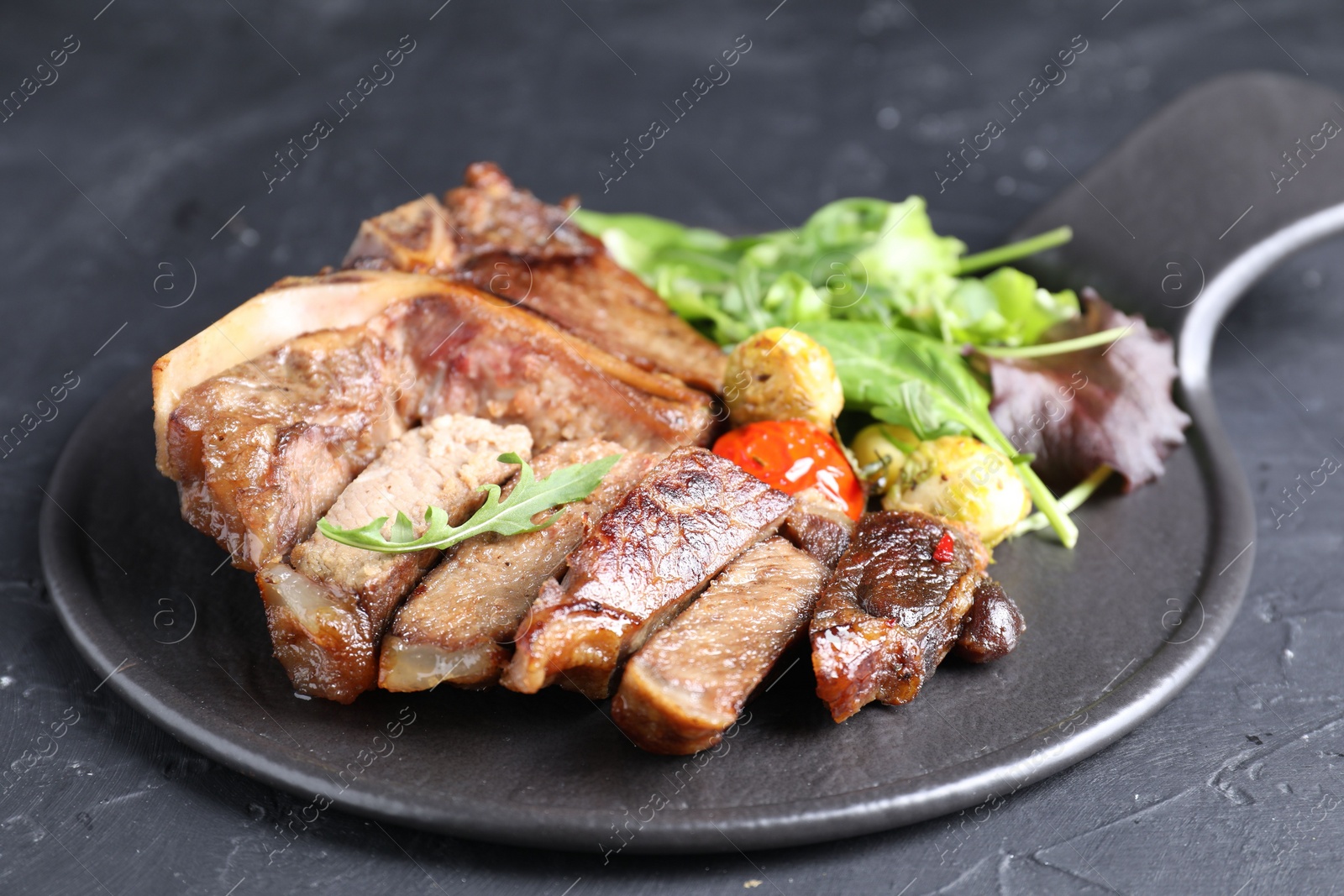 Photo of Delicious grilled beef meat, vegetables and greens on black table, closeup