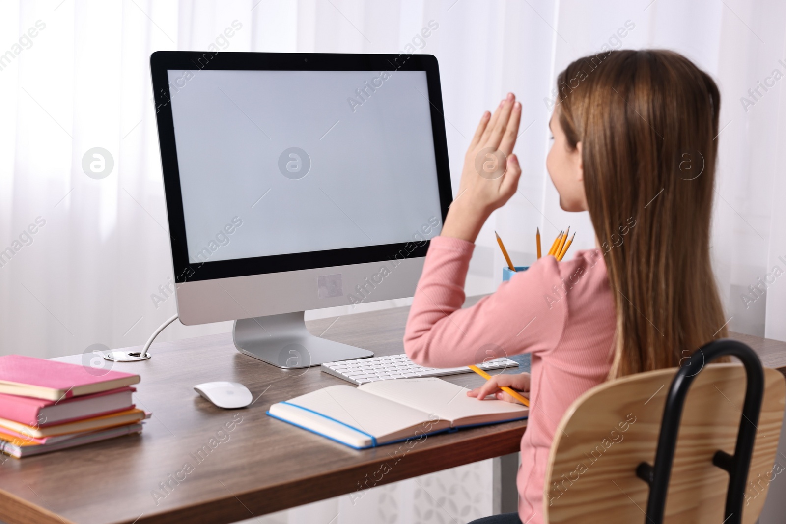 Photo of E-learning. Girl raising her hand to answer during online lesson at table indoors