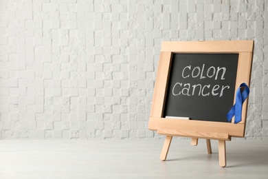 Photo of Chalkboard with blue ribbon and text Colon cancer awareness on table