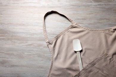 Photo of Stylish beige apron and spatula on light wooden table, top view. Space for text