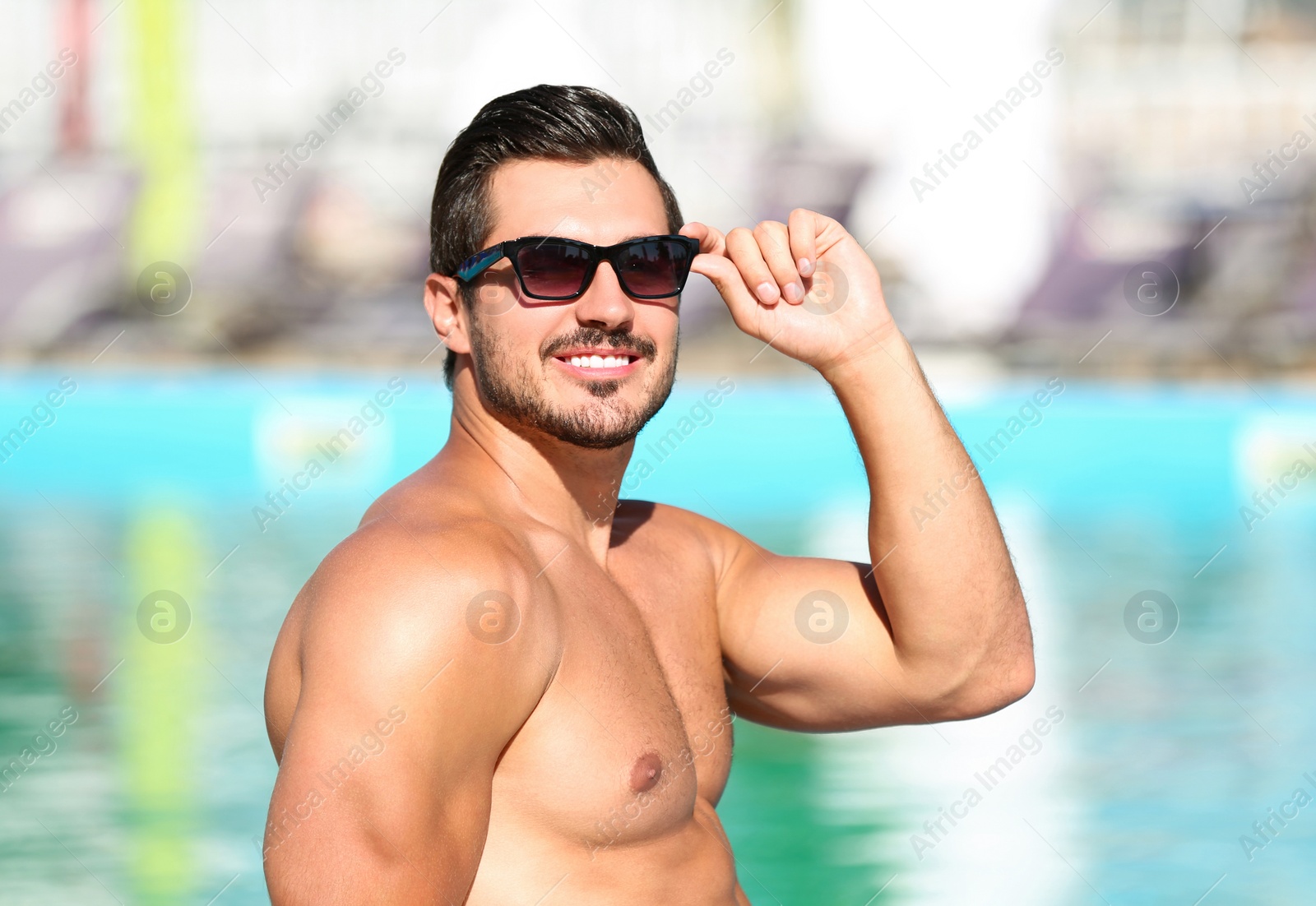 Photo of Handsome young man with sunglasses near swimming pool on sunny day