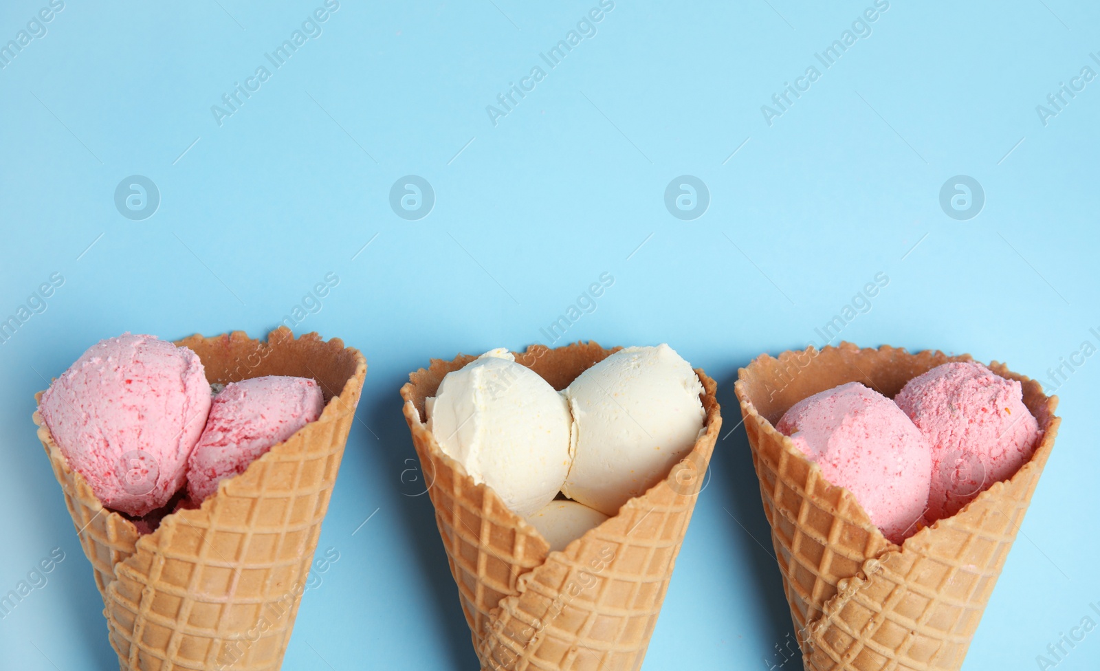 Photo of Delicious ice creams in wafer cones on blue background, flat lay. Space for text