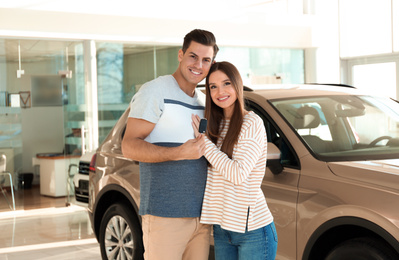 Happy couple with car key in modern auto dealership