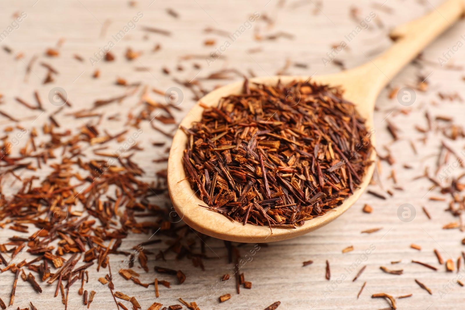 Photo of Spoon with dry rooibos leaves on wooden table, closeup