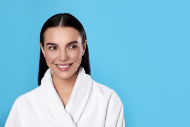 Photo of Portrait of attractive young woman in bathrobe on light blue background, space for text. Spa treatment