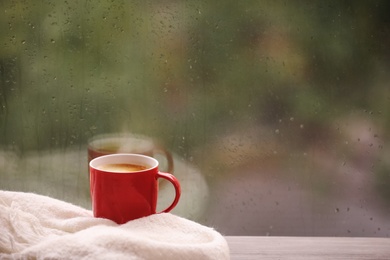 Photo of Cup of drink and blanket on windowsill, space for text. Rainy weather