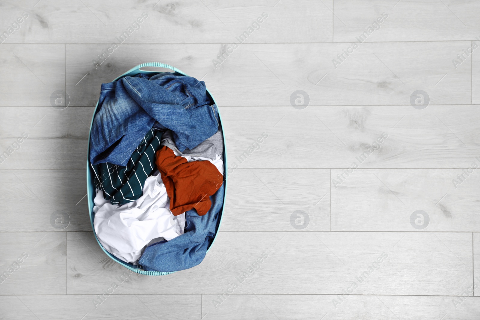 Photo of Laundry basket full of dirty clothes on floor, top view. Space for text