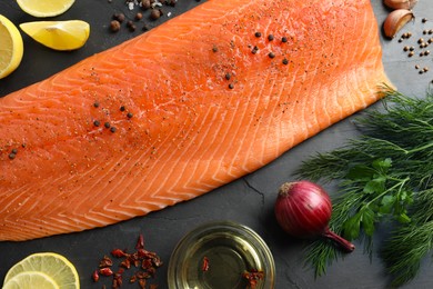 Fresh raw salmon and ingredients for marinade on black table, flat lay