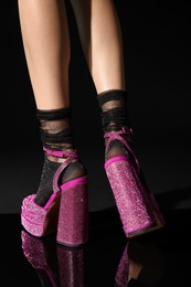 Woman wearing pink high heeled shoes with platform and square toes on black background, closeup