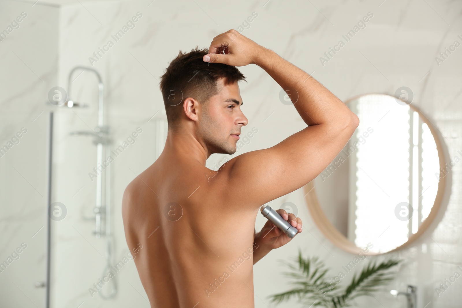 Photo of Young man applying fresh deodorant to armpit in bathroom