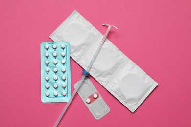 Contraception choice. Pills, condoms and intrauterine device on magenta background, flat lay