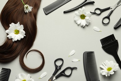 Flat lay composition with professional hairdresser tools, flowers and brown hair strand on light grey background. Space for text