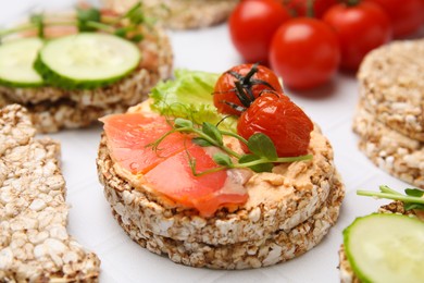 Photo of Crunchy buckwheat cakes with salmon, tomatoes and greens on white table, closeup