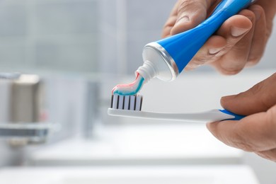 Photo of Man applying toothpaste on brush in bathroom, closeup. Space for text