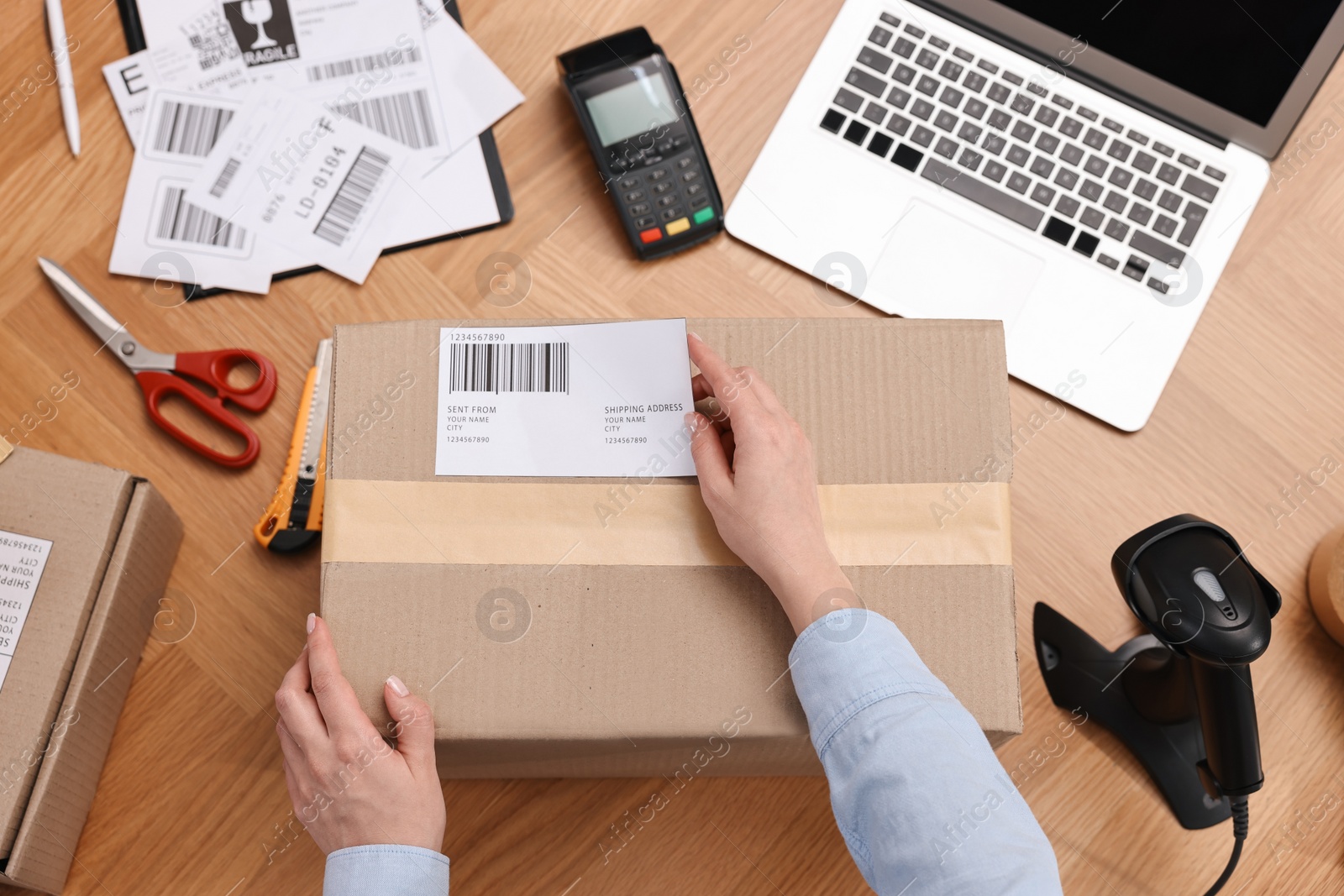 Photo of Parcel packing. Post office worker sticking barcode on box at wooden table, top view