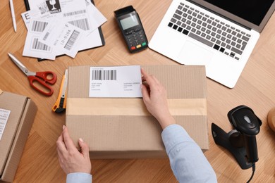 Parcel packing. Post office worker sticking barcode on box at wooden table, top view