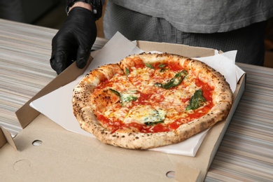 Professional chef with Italian oven baked pizza at table in restaurant, closeup