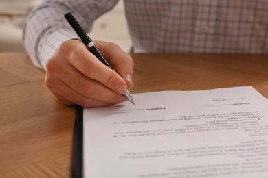 Photo of Businessman signing contract at wooden table, closeup of hands