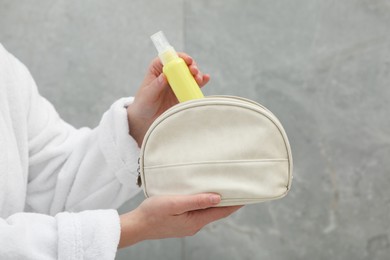 Photo of Woman packing cosmetic travel kit near grey wall closeup. Bath accessories