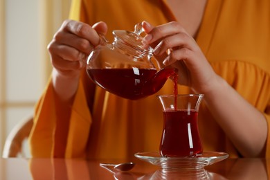 Photo of Woman pouring tasty Turkish tea into glass at table, closeup