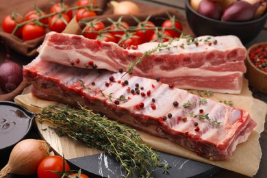 Photo of Raw pork ribs with thyme and peppercorns on table, closeup