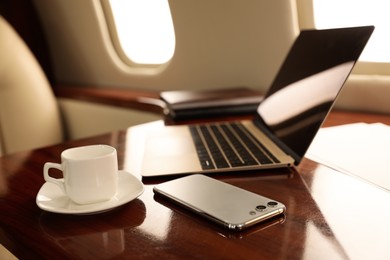 Photo of Cup of coffee with laptop and smartphone on table in airplane