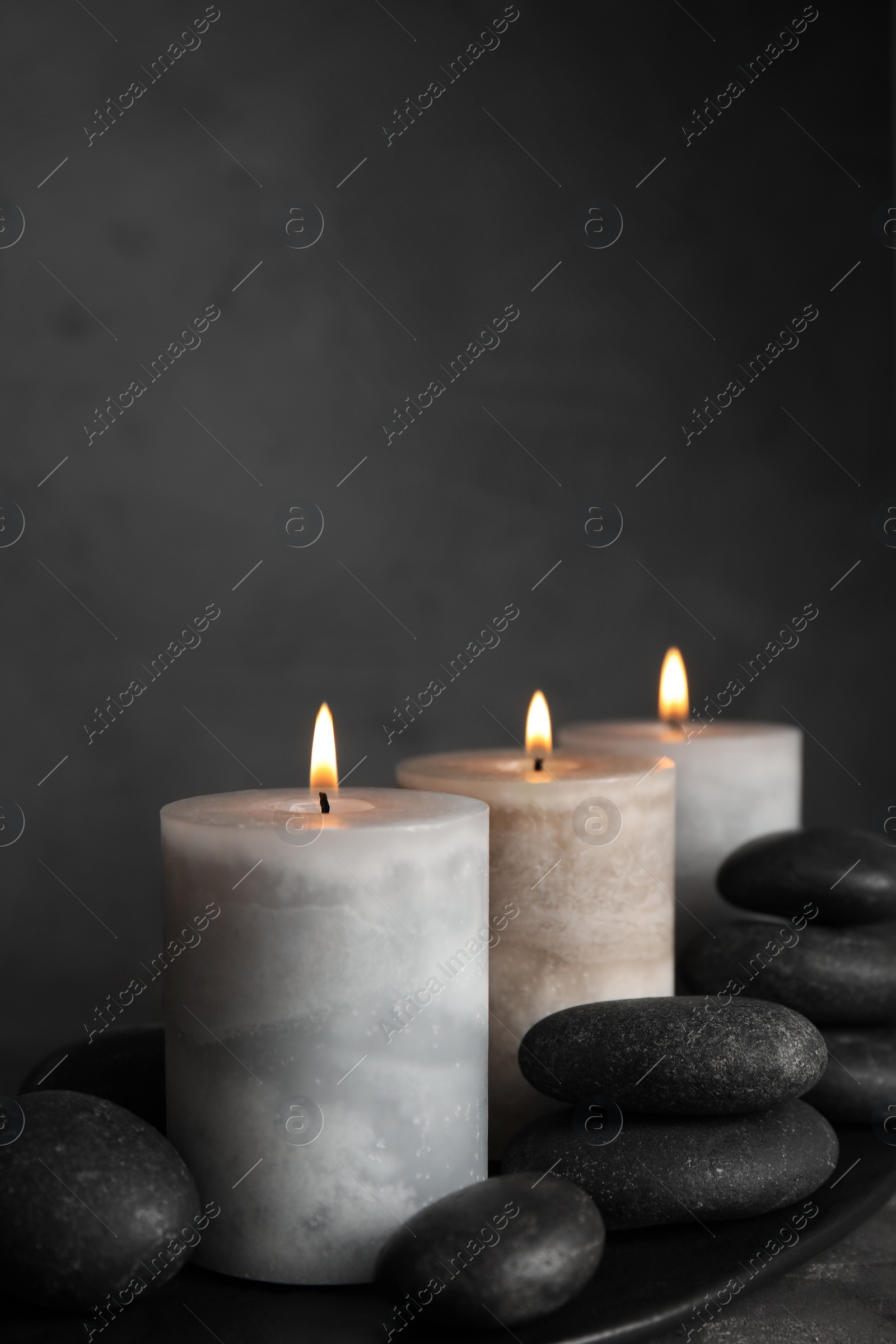 Photo of Burning candles and spa stones on black plate, space for text