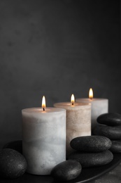 Photo of Burning candles and spa stones on black plate, space for text