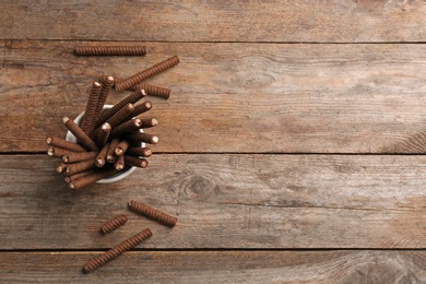 Bowl of delicious chocolate wafer rolls on wooden table, top view with space for text. Sweet food