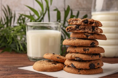 Photo of Stack of delicious chocolate chip cookies and milk on wooden table. Space for text
