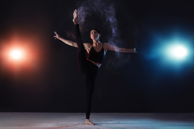 Professional acrobat with chalk powder exercising in dark studio