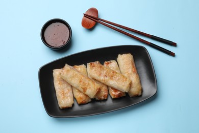 Photo of Fried spring rolls and sauce served on light blue table, top view