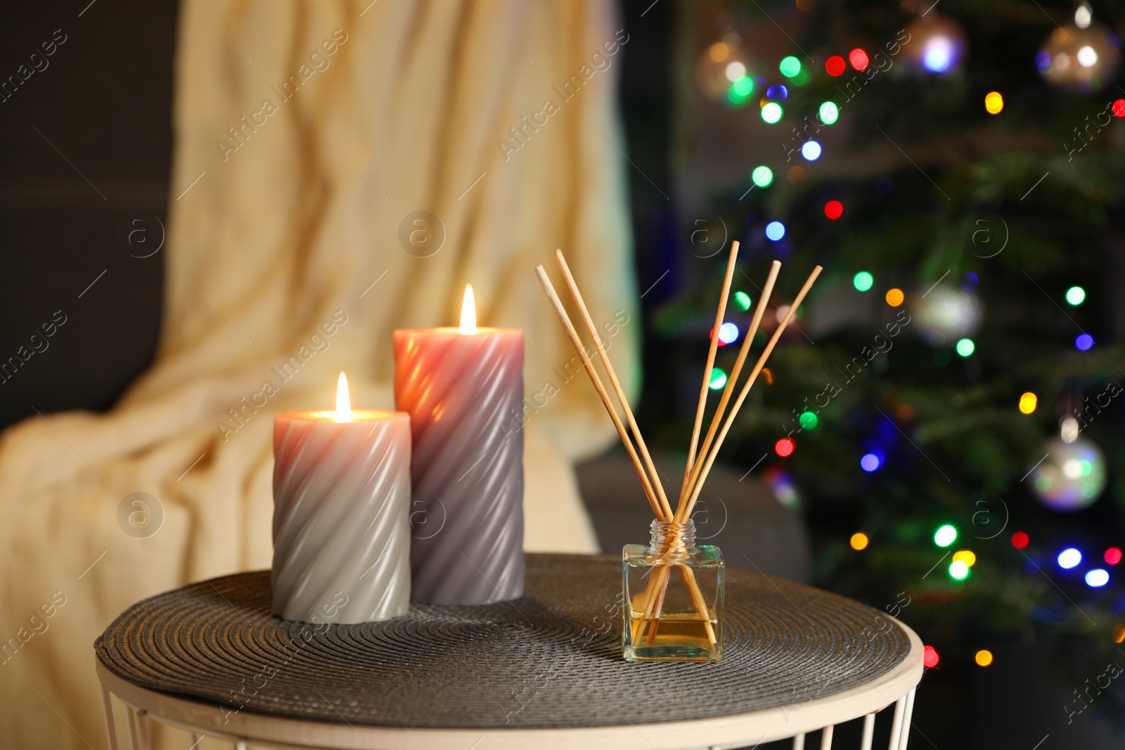 Photo of Aromatic reed air freshener and candles on side table in cozy room