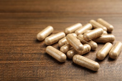 Photo of Dietary supplement capsules on wooden table, closeup. Space for text